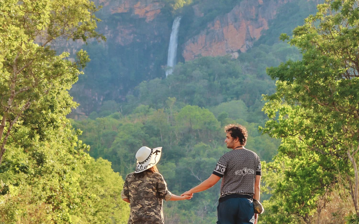 Casal de mãos dadas na estrada de acesso, com o Salto do Itiquira ao fundo entre as encostas